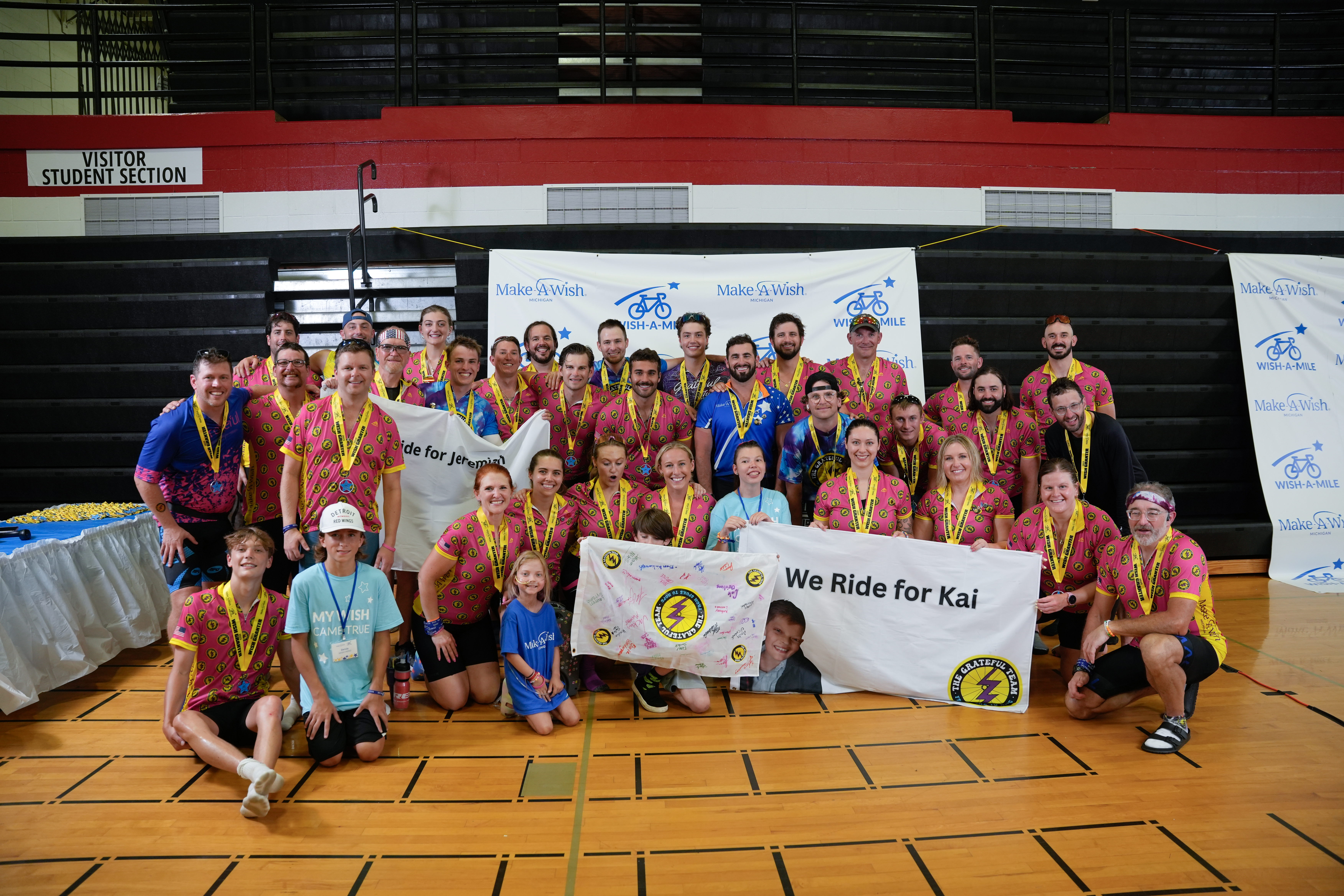 The Grateful Team after a Wish-A-Mile ride, posing together with 'We Ride for Kai' and 'We Ride for Jeremiah' banners
